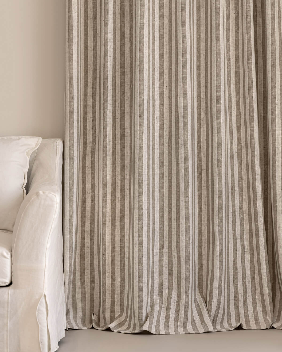 The Colette taupe striped curtains and a matching pillow styled with a white slipcovered sofa.