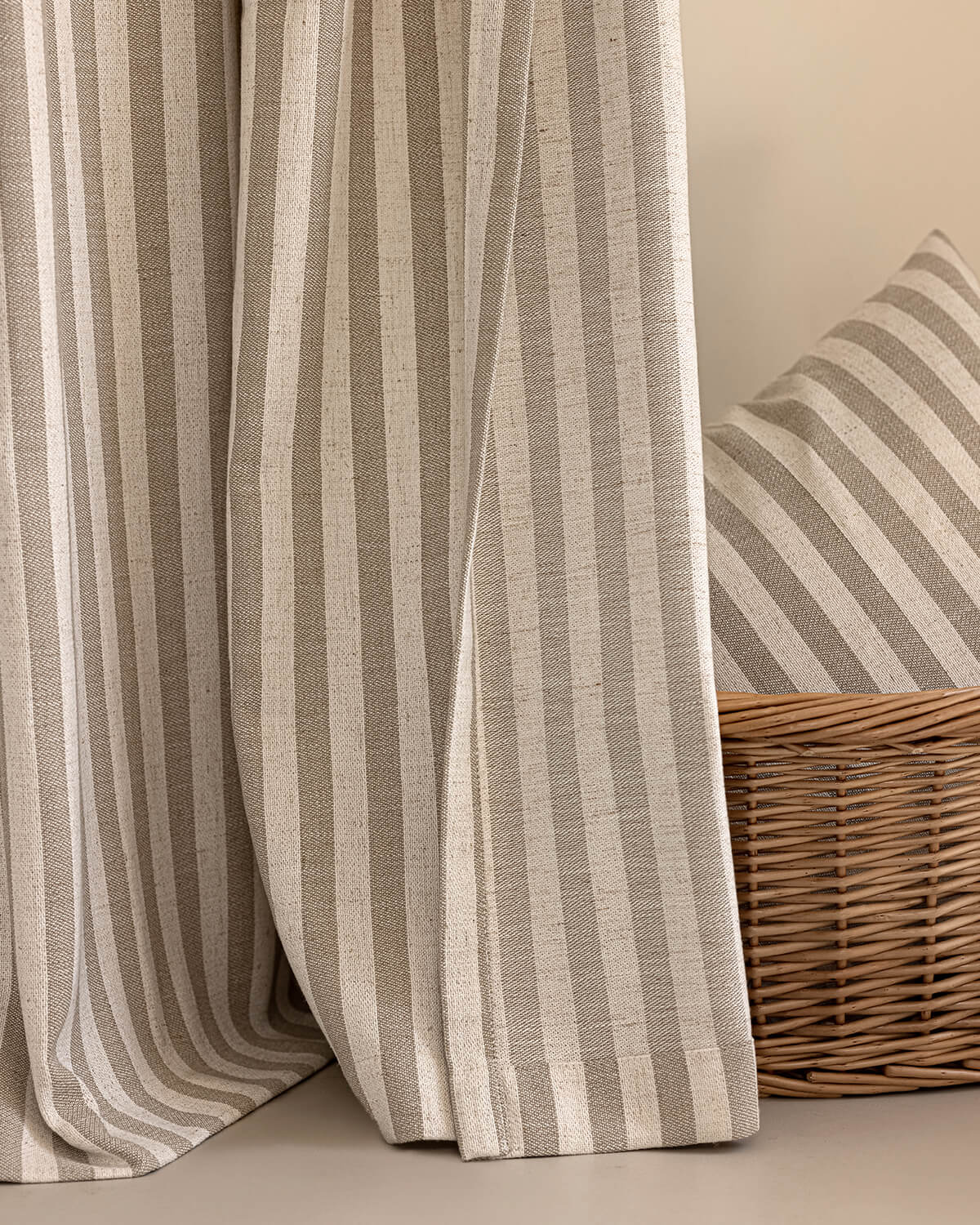 A close-up of the Colette taupe striped linen blend curtain with a matching pillow in a basket.