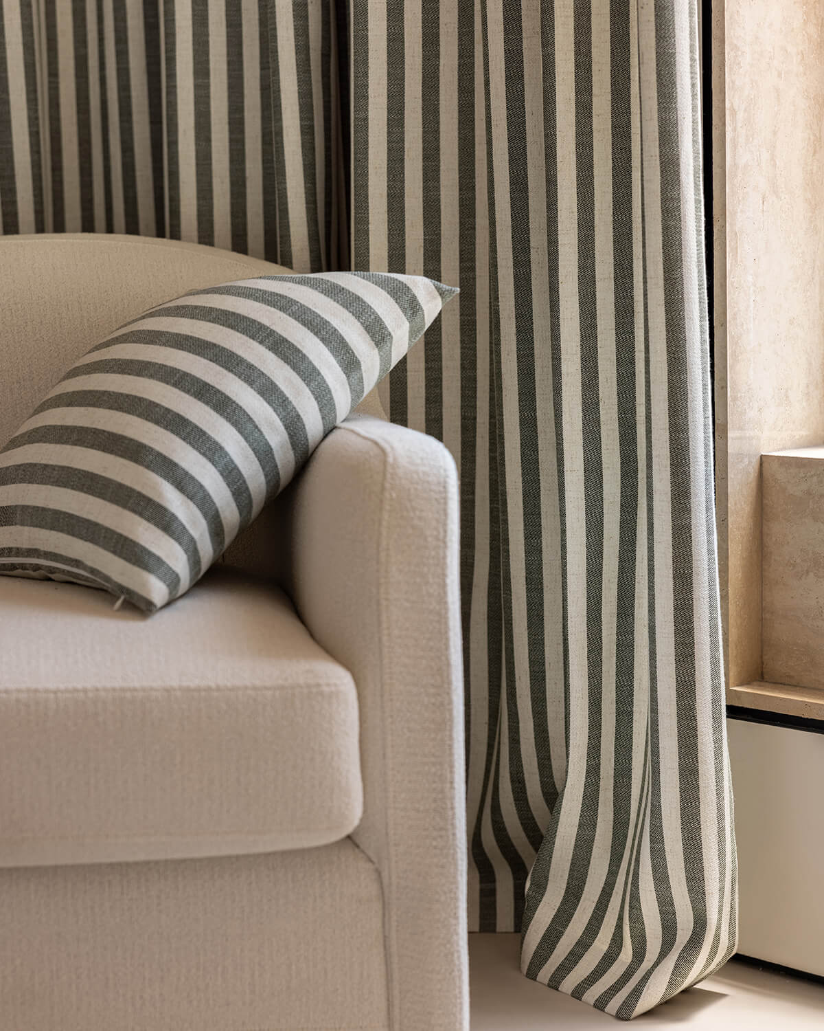 The Colette charcoal striped curtain and a matching pillow on a modern cream armchair.