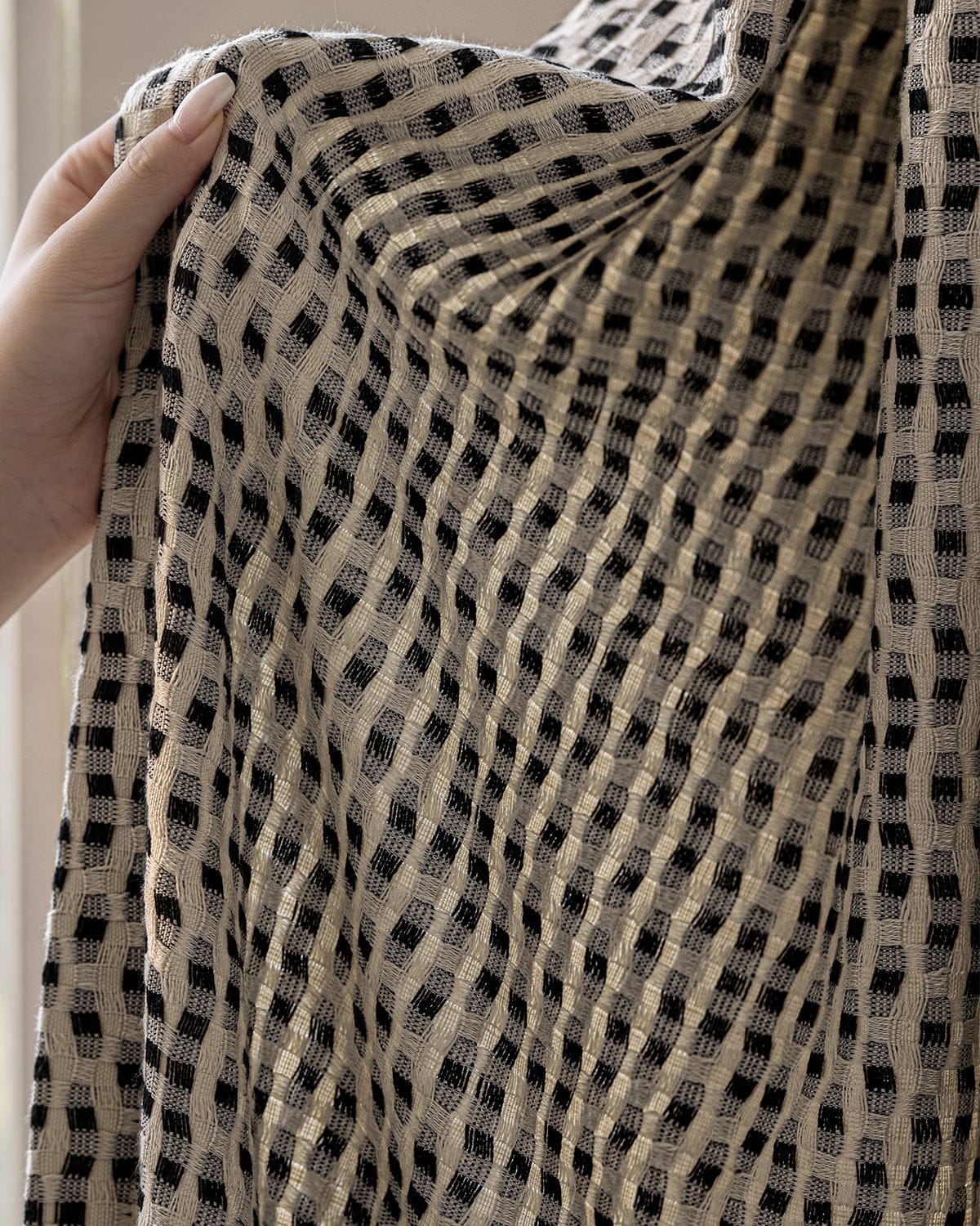 A hand holding the black and cream Elise curtain to the light, showing its knitted texture.