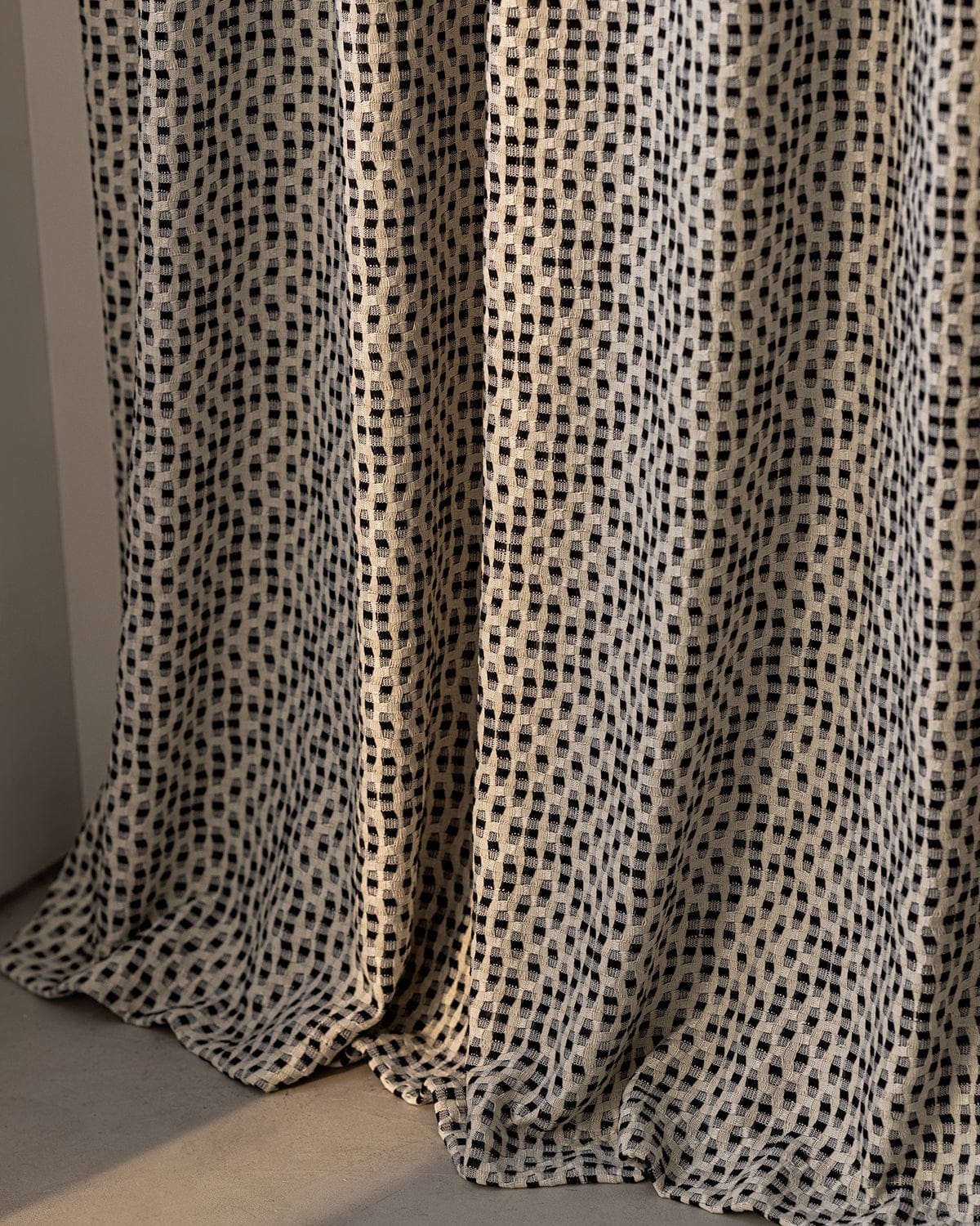 A close-up of the drape and textured plaid pattern of the Elise curtain in black and cream.