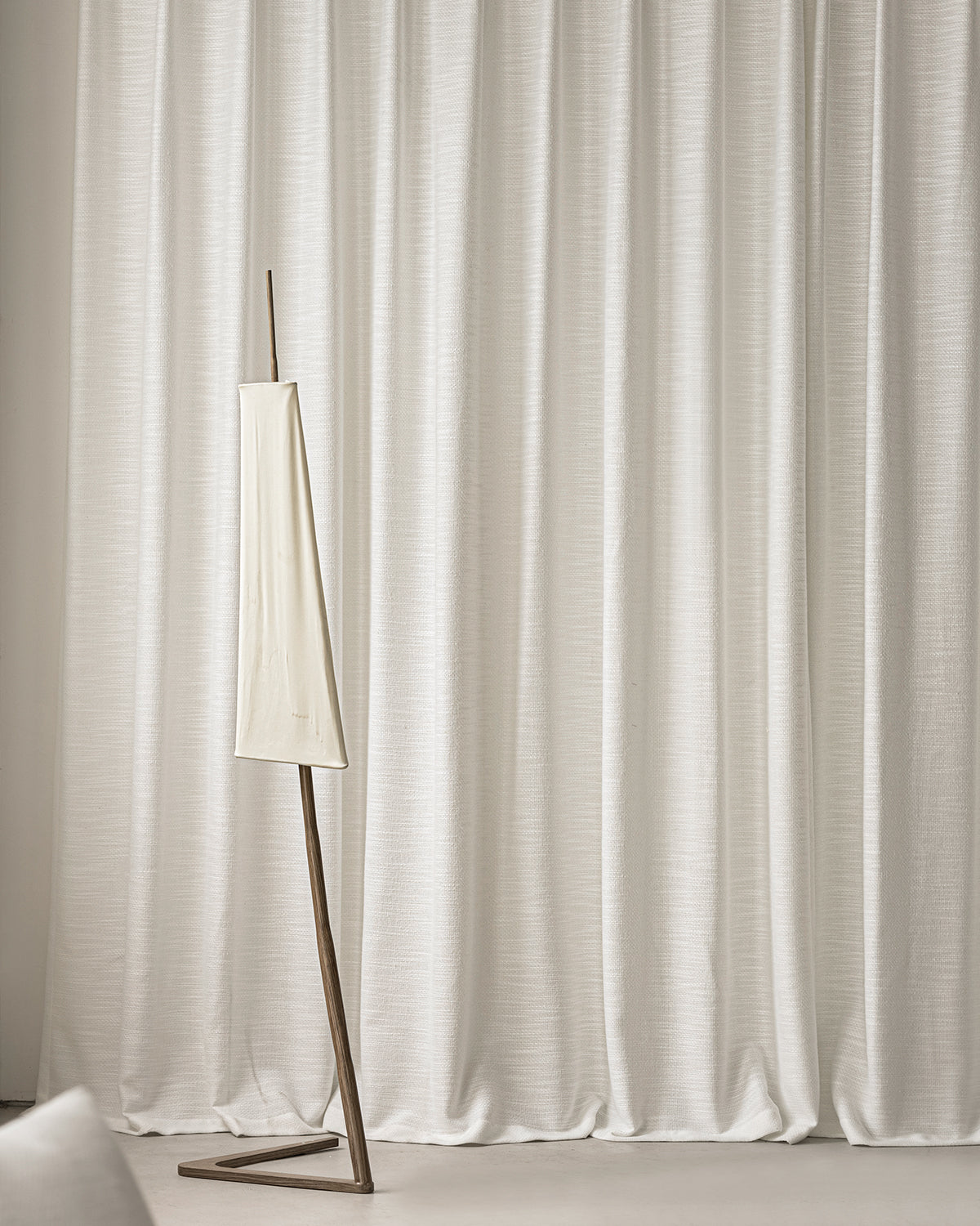 A full wall of the Sophie supple curtains in off-white behind a modern floor lamp.