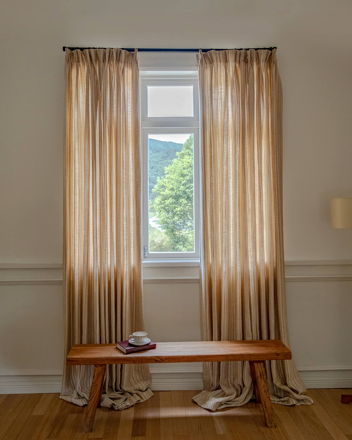 A pair of Thea striped pinch pleated curtains symmetrically framing a window above a wooden bench.