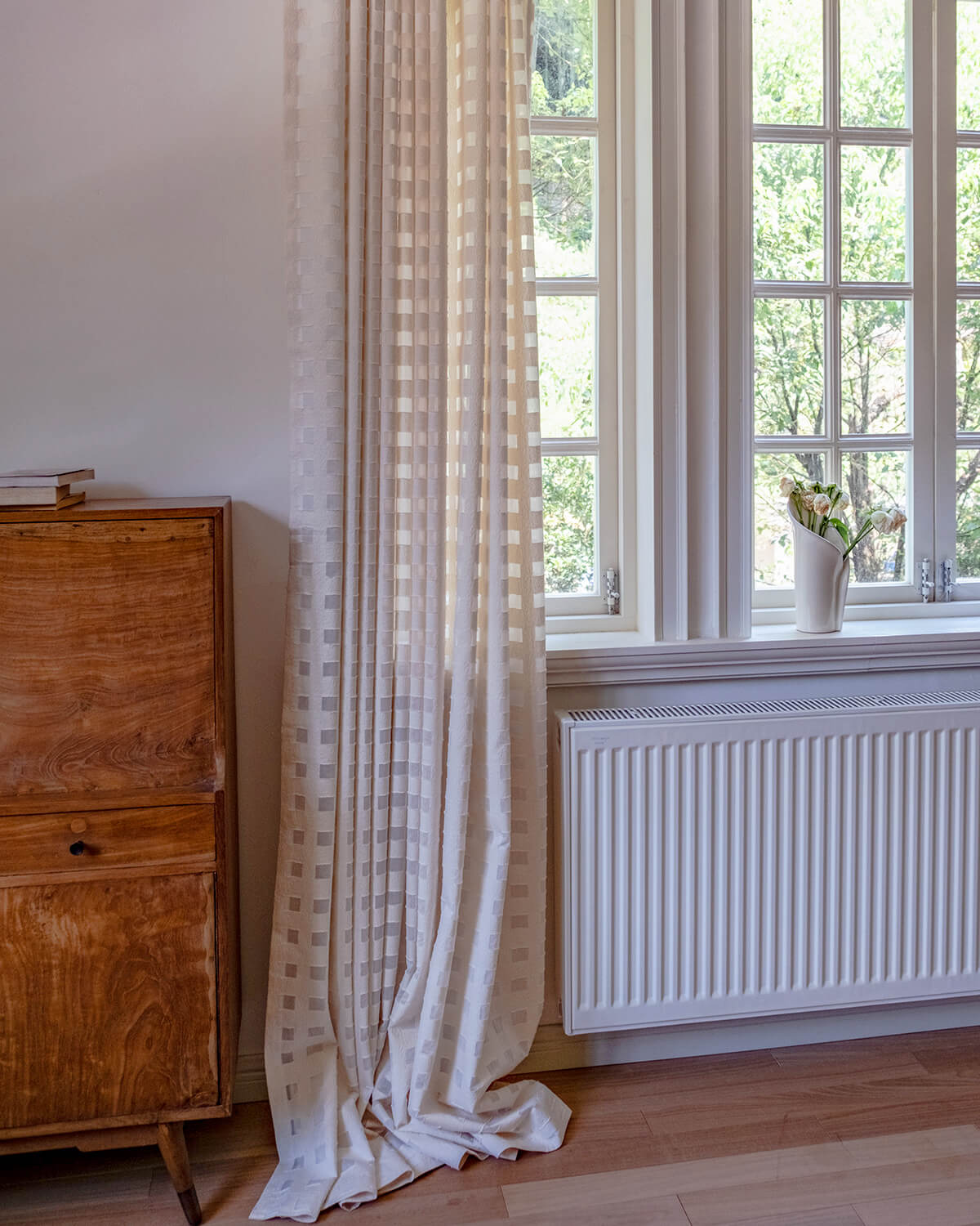 A single panel of the Aria textured check curtain puddling on the floor beside a window.