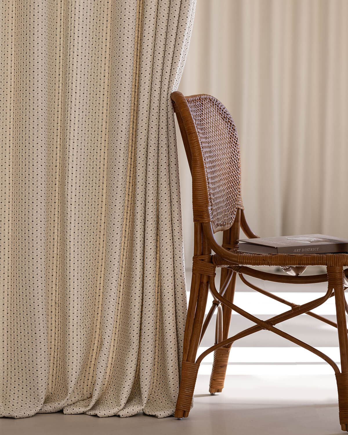 The heavyweight Motti textured curtain hanging gracefully next to a natural rattan chair.
