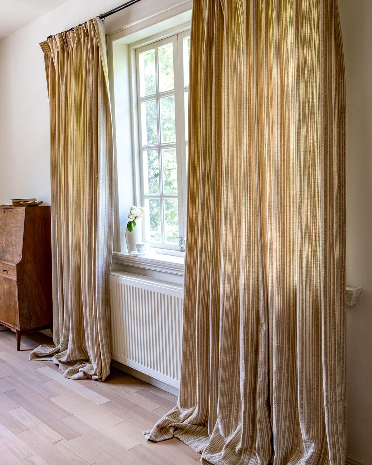 A pair of Thea striped pinch pleated curtains framing a window with a view of green mountains.