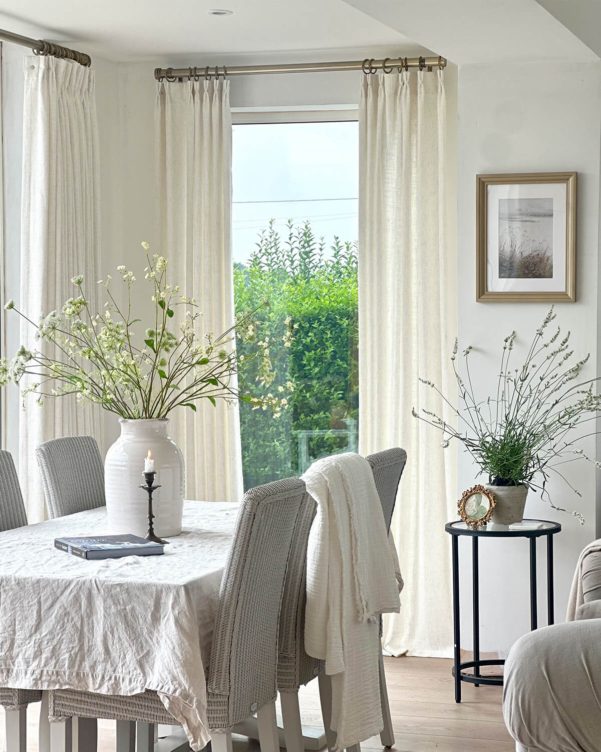 The Clara off-white curtain hanging by a dining table with a view of a green field.