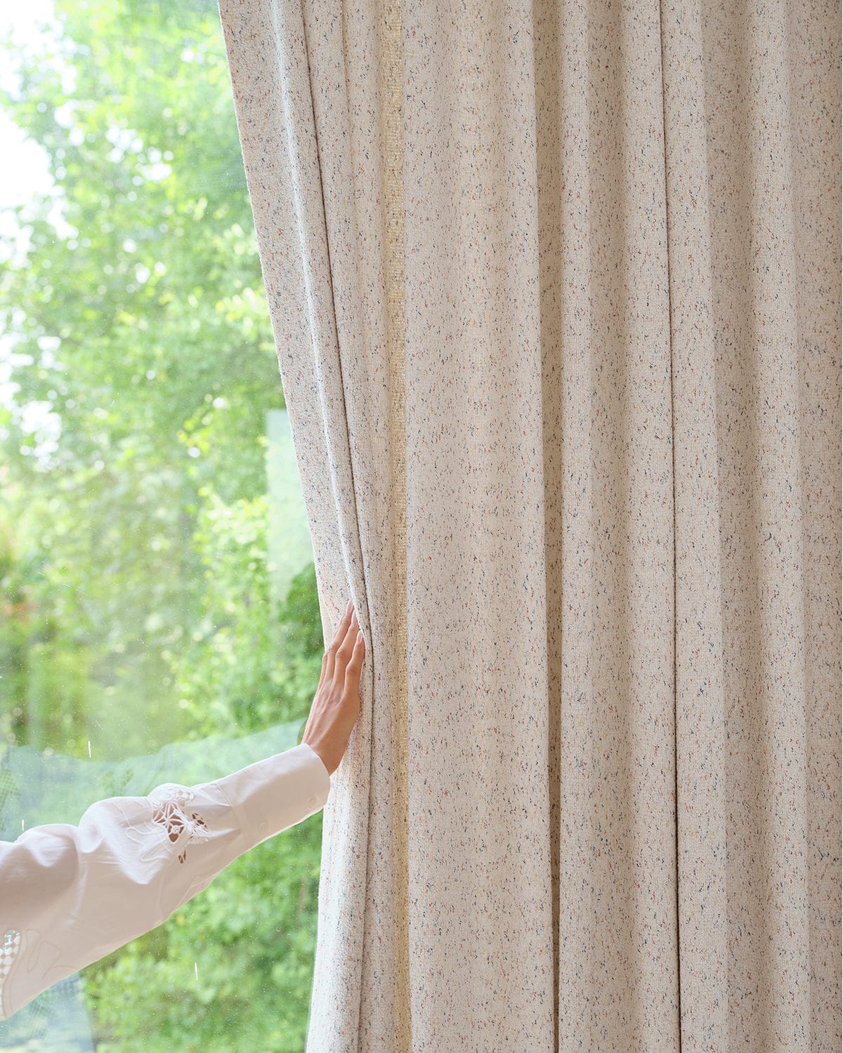 A hand touching the edge of the Juno speckle curtain, showing its heavyweight drape.