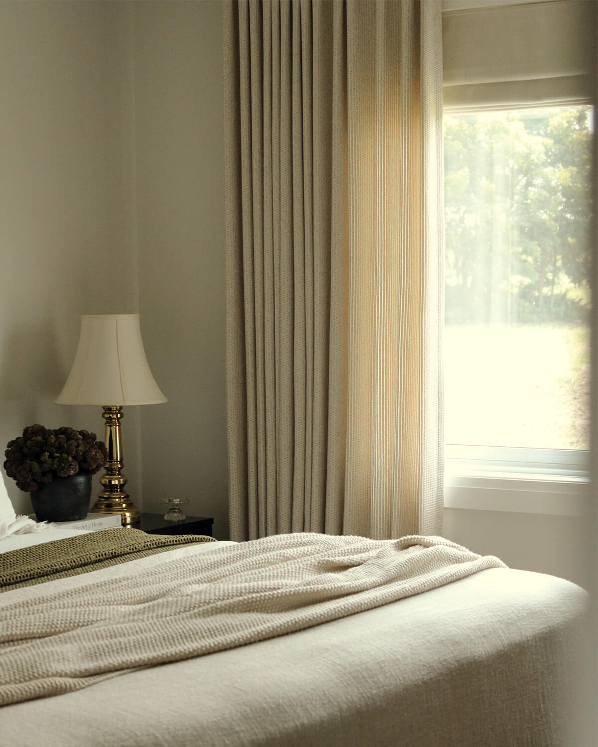 The beige Margot light-filtering drape hanging beside a window in a cozy bedroom.