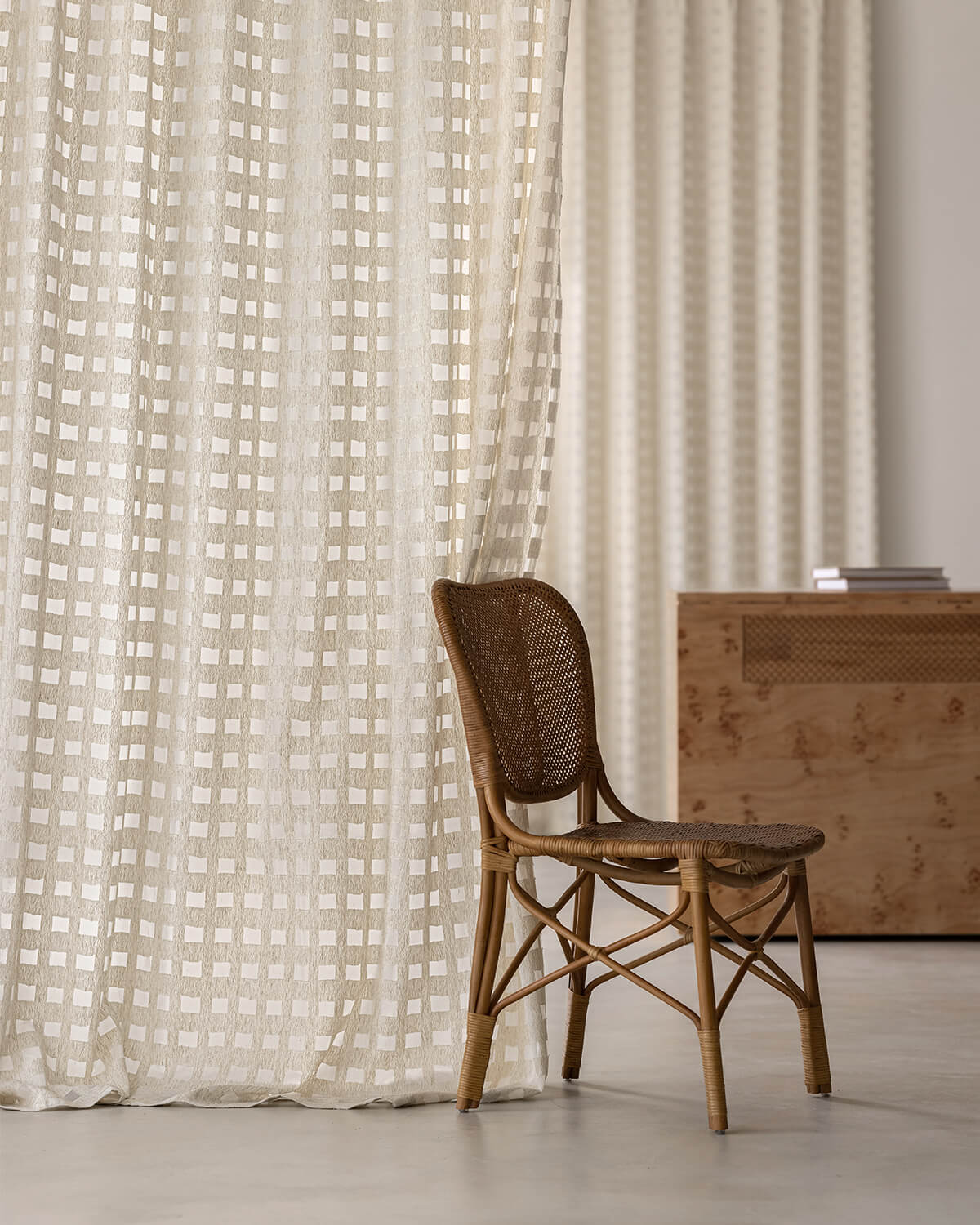 The Aria sheer cotton check curtain hanging as an elegant backdrop behind a rattan chair.