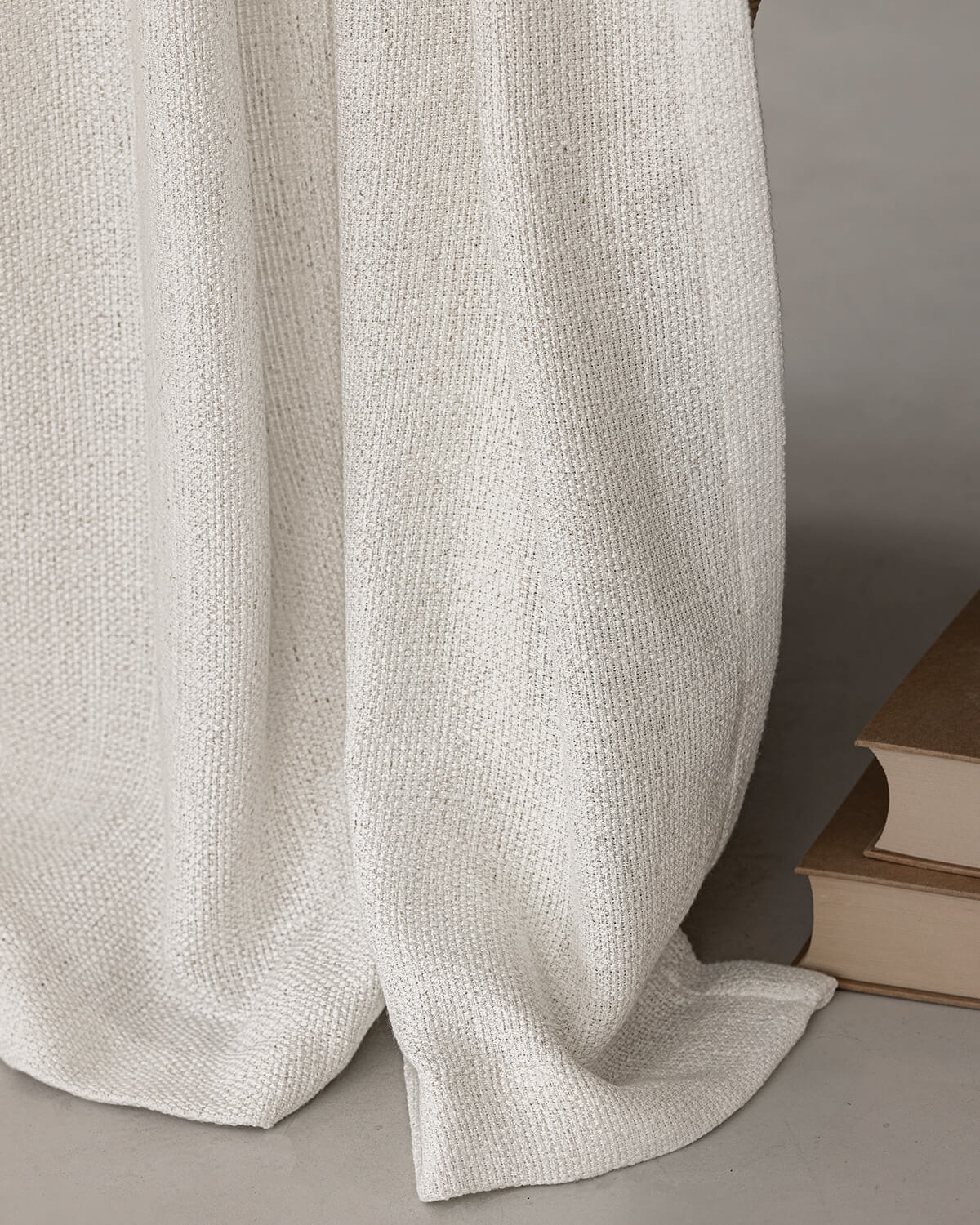 A detail shot of the richly textured, off-white Clara curtain fabric draped on the floor.