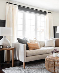 Luma herringbone linen blend curtains hanging on a black rod in a modern living room with a white boucle chair.