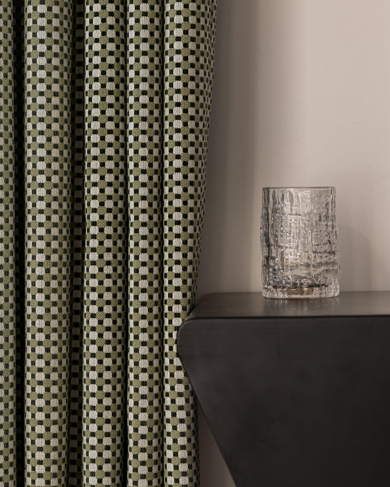The heavyweight Frankie plaid curtain draped elegantly beside a modern black side table.