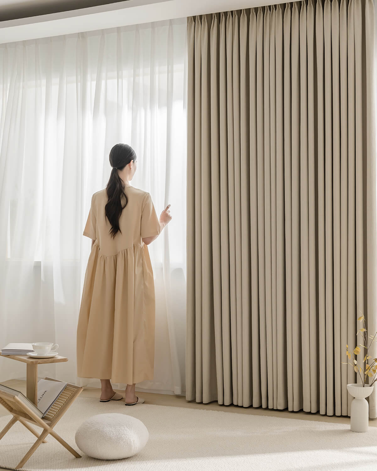 A woman walking past a large window dressed with Fuzz beige Chenille blackout curtains.