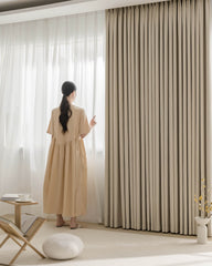 A woman walking past a large window dressed with Fuzz beige Chenille blackout curtains.