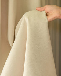 A hand holding the Mell beige Chenille blackout fabric to demonstrate its drape and softness.