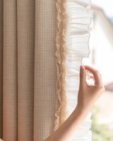 Close-up hand touching the delicate sheer ruffle trim on the edge of thick beige waffle weave curtains.