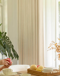 A close-up of a hand holding a red apple next to the Mell beige Chenille blackout curtain.