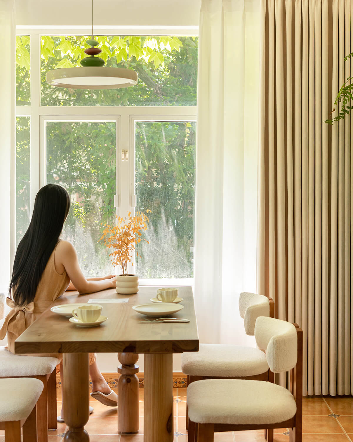 A woman sitting at a dining table with Mell beige Chenille blackout curtains in the background.
