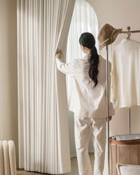 A person in loungewear opening the thick Kely Chenille curtains to let soft light into a bright room.