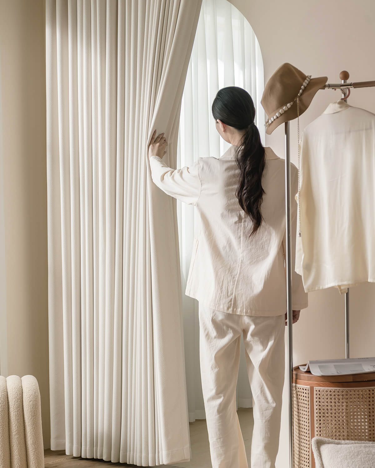 A person in loungewear opening the thick Kely Chenille curtains to let soft light into a bright room.