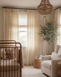Pinch pleat Darcy Striped Beige Curtains in a stylish nursery with a brass crib and beaded chandelier.