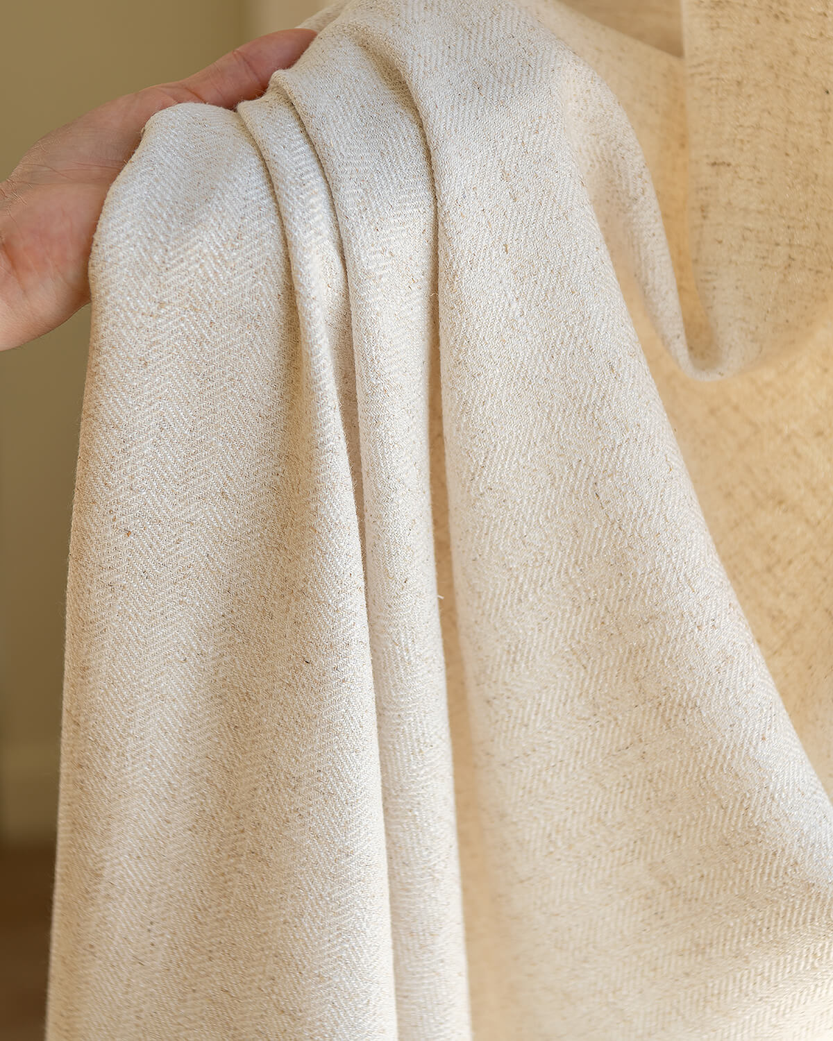 A hand holding the edge of the Tina curtain, highlighting its thick weight and premium linen blend quality.