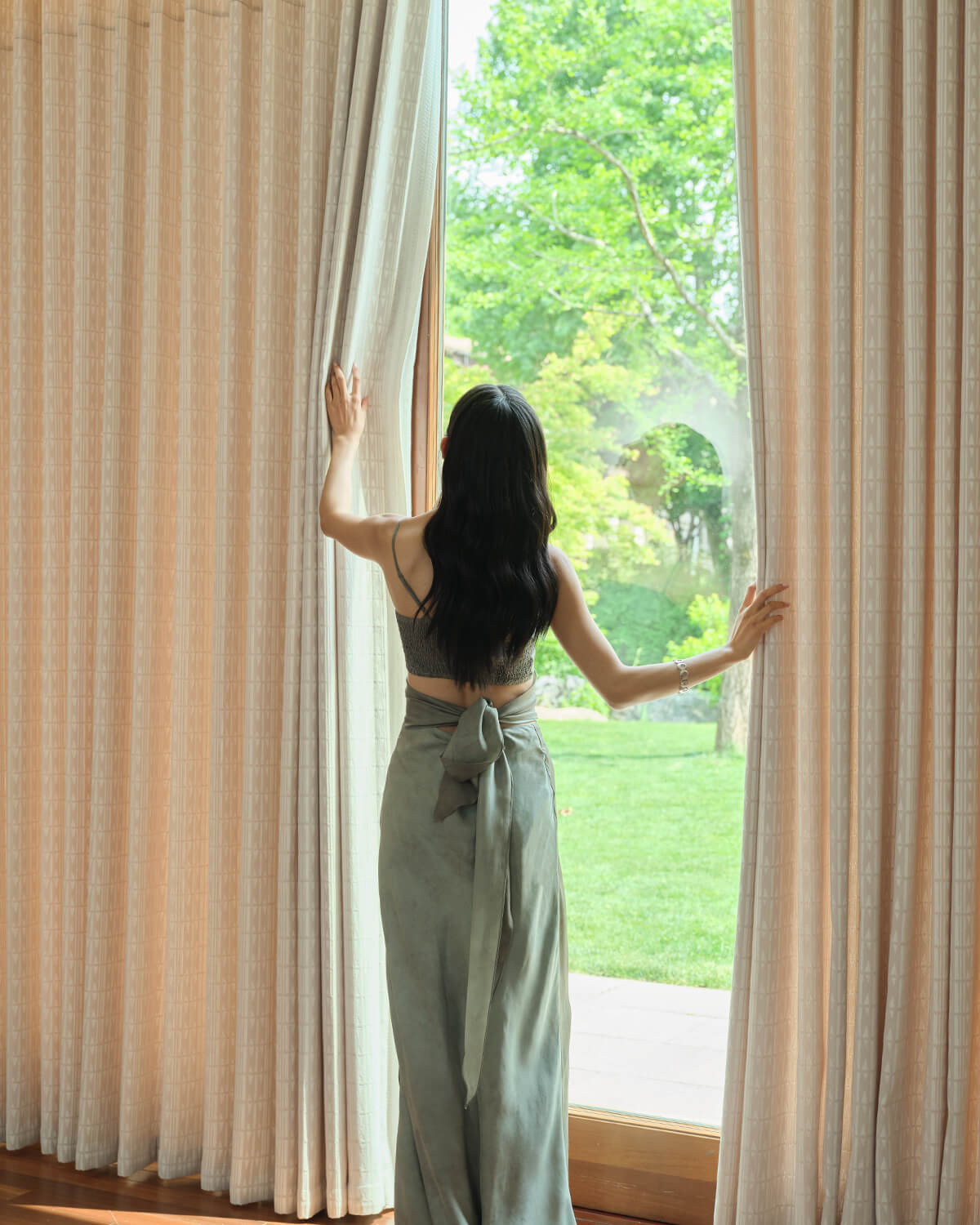 A woman opening the heavyweight Celia jacquard curtains to reveal a beautiful garden view.