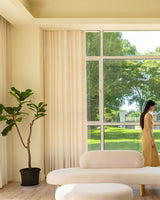 Thick beige linen blend pinch pleated drapes filtering natural light in a modern living room with large windows.