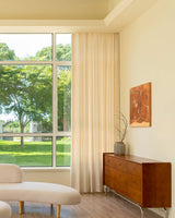 Elegant cream solid pattern linen curtains showing heavy 428gsm fabric texture and drape next to wooden furniture.