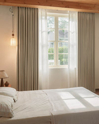 Vivi Chenille blackout curtains hanging in a sunlit bedroom with wooden ceiling beams, showcasing their elegant drape and texture.