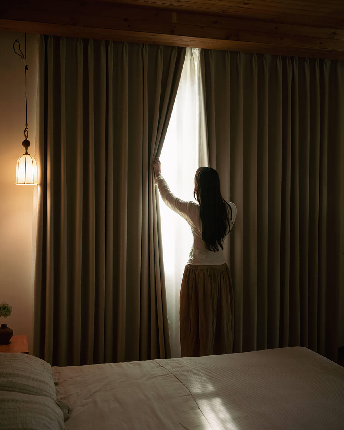A person pulling back the heavy Vivi Chenille blackout curtains in a bedroom, demonstrating their exceptional light-blocking performance.